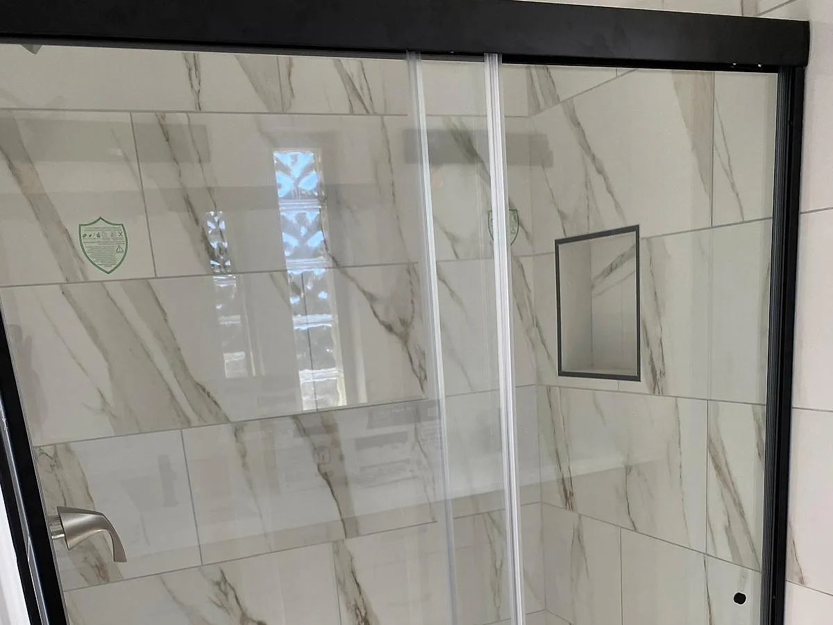 Walk-in shower with white veined stone walls and a glass enclosure