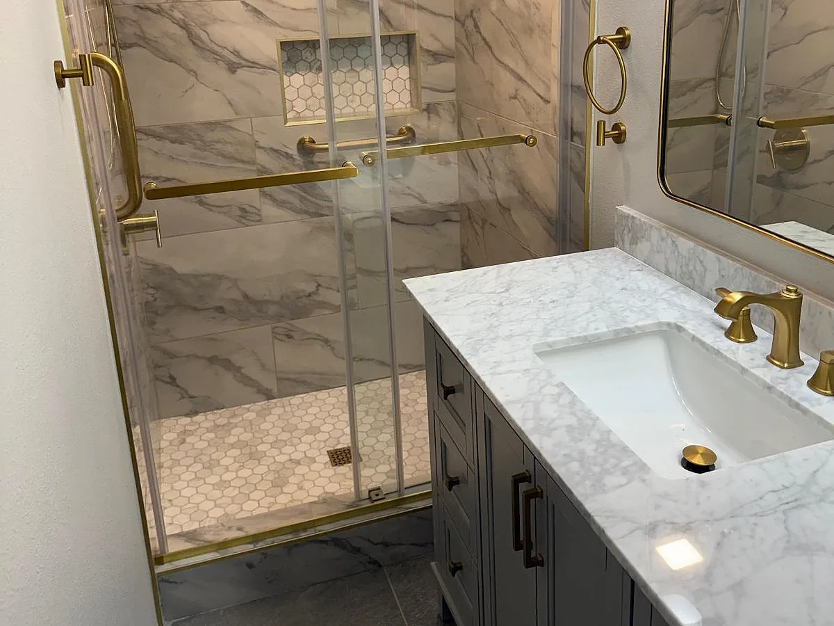 Marble-tiled walk-in shower with gold fixtures and a stone vanity top
