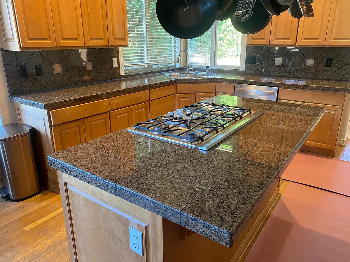 Deep-toned granite island with a gas cooktop in a wood-cabinet kitchen