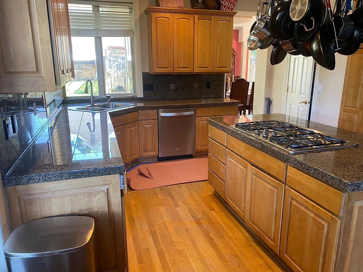 Dark granite island with a gas cooktop and bar seating in a wood-cabinet kitchen