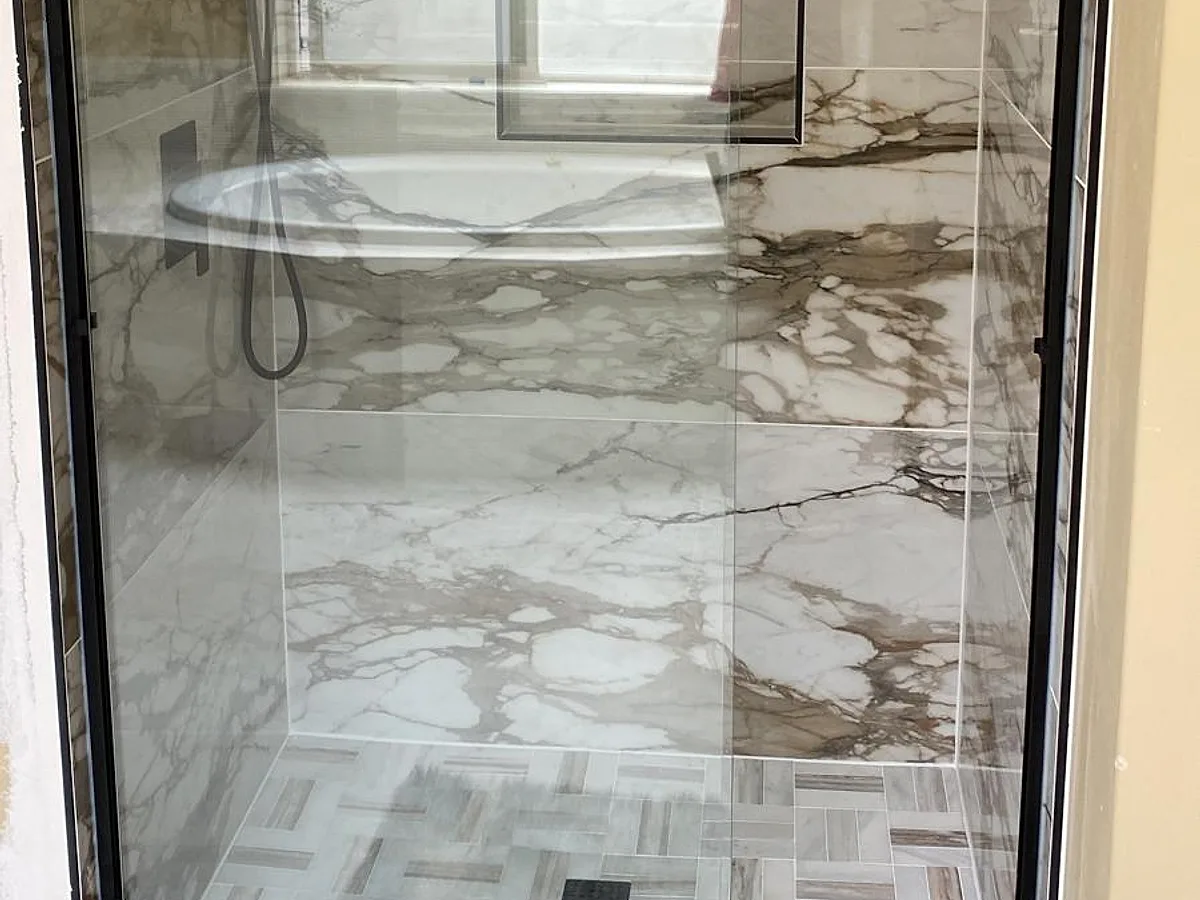 Frameless glass shower enclosure with large-format marble-look walls