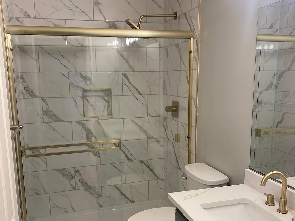 Marble-tiled shower with a glass enclosure and stone-topped vanity